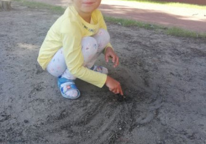 dziewczynka rysuje patykiem na piasku